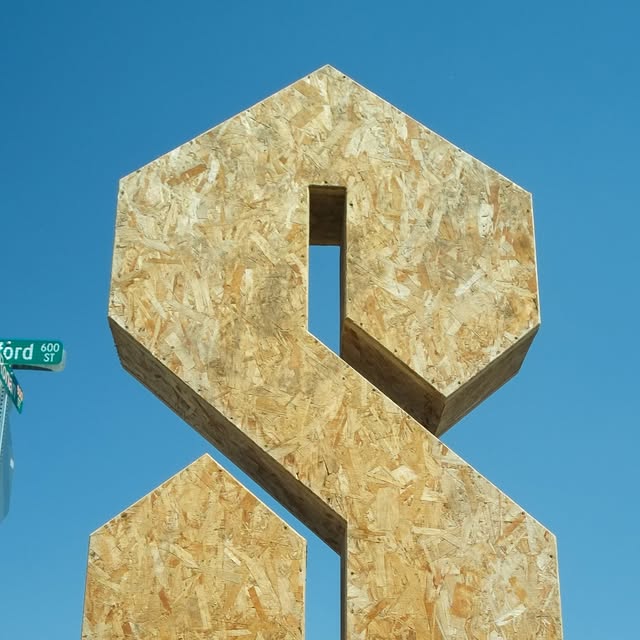 The S, a large geometric S-shaped sculpture made of oriented strand board, against a blue sky